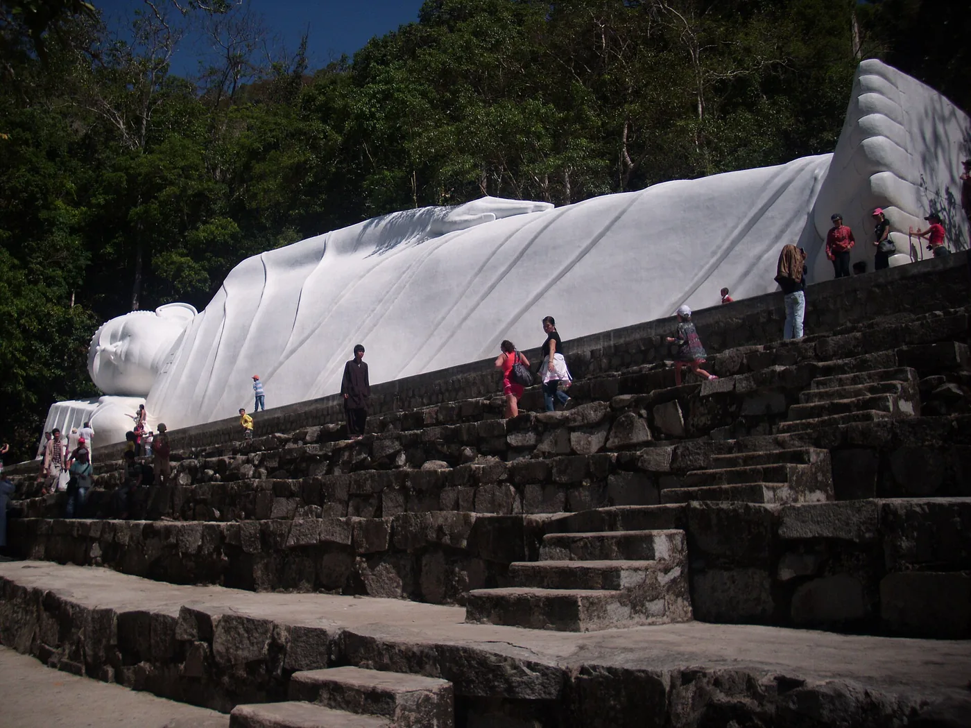 The white reclining Buddha on Ta Cu mountain with visitors on the stone steps below it The white reclining Buddha on Ta Cu mountain with visitors on the stone steps below it